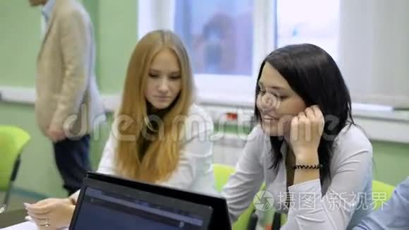 学生们在教室里看笔记本电脑。 练习经济学课。 黑发女孩微笑。