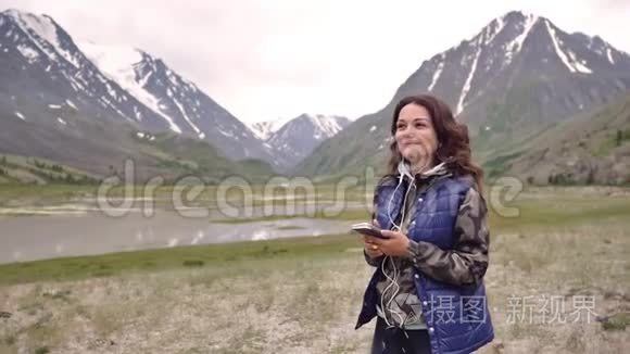 女游客戴着耳机在群山和风景的背景下跳舞。 旅游观光