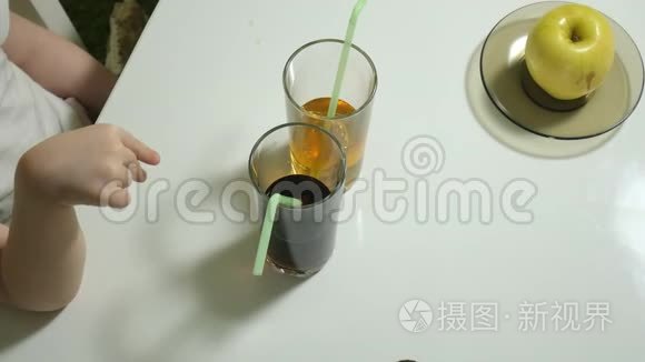 一个可爱的小女孩坐在一张桌子旁，选择喝什么，可乐或果汁，健康生活方式的概念