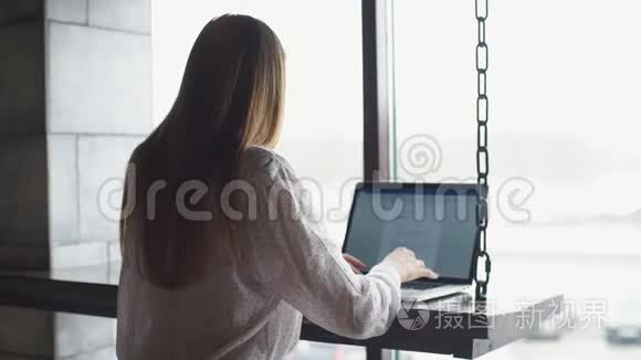 年轻的女商人穿着白色衬衫，坐在电脑前的木桌旁的咖啡馆里，在手机上聊天