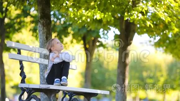 可爱的小女孩在美丽的秋日户外。 秋天，可爱的孩子坐在户外公园的长凳上