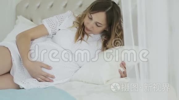 美丽的孕妇在家里躺在床上摆姿势。