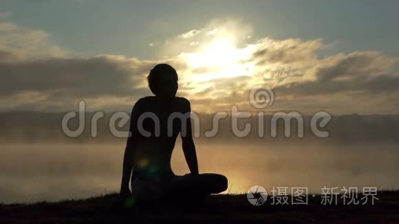 年轻人坐在湖畔，在日落时慢动作练习瑜伽