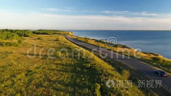 夏季日落时沿着海边的悬崖在公路上驾驶黑色汽车的鸟瞰图。