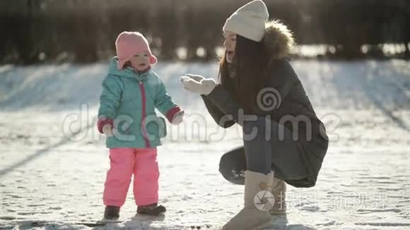 年轻的母亲在手里吹雪，小女儿在看雪花。 女孩子在玩