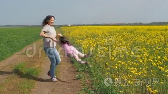 那个女人正在转动婴儿。 妈妈和女儿在大自然中。 开着黄花的幸福家庭。 油菜田。