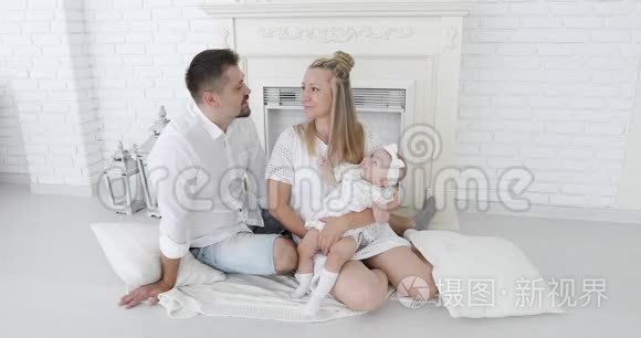 一对幸福的夫妇和一个小女儿坐在白色壁炉旁接吻。