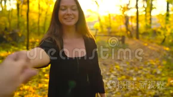 美丽的女孩牵着男朋友的手，跟着他穿过黄色的秋天森林。