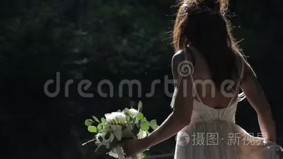 新娘在婚礼阳光日慢动作时带着花束漫步公园