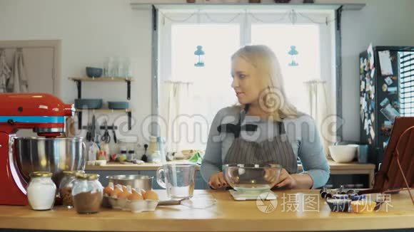 年轻的金发女人用厨房的秤称面粉。 漂亮的女人在厨房烤蛋糕。