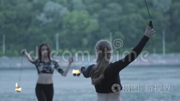 两个年轻女子站在河岸上表演火焰球。 熟练的火技艺术家表现出娴熟的技巧
