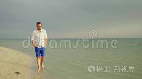 一个年轻漂亮的男人，穿着浅色的衣服和眼镜。 沿着海边走。 摆脱忧虑，自由