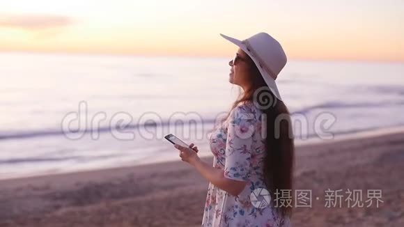 戴帽子的年轻女游客在海洋海滩日落时拍照