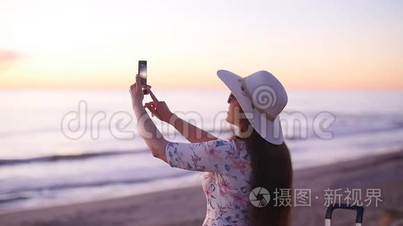 戴帽子的年轻女游客在海洋海滩日落时拍照