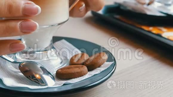 装有咖啡的玻璃烧杯，由深棕色分级为乳白色.. 漂亮的拿铁，咖啡馆里有一个大泡沫。 一个女人