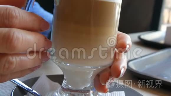 装有咖啡的玻璃烧杯，由深棕色分级为乳白色.. 漂亮的拿铁，咖啡馆里有一个大泡沫。 一个女人