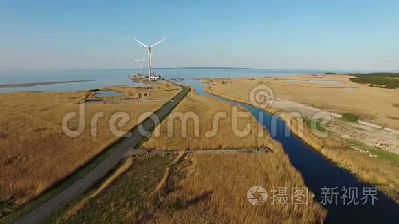 4K.可旋转风力涡轮机、蓝色河流、田野和海边道路的鸟瞰图