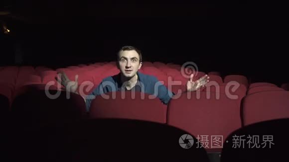 一个人坐在黑暗的电影院里舒适的红椅子上，看着演出，忧心忡忡