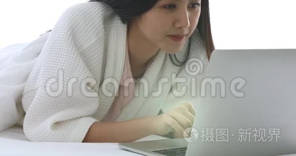 漂亮的亚洲女人在床上用笔记本。
