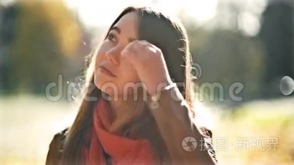 年轻美丽的女人在阳光明媚的日子里看着镜头，秋天的背景。 微笑快乐女孩肖像。