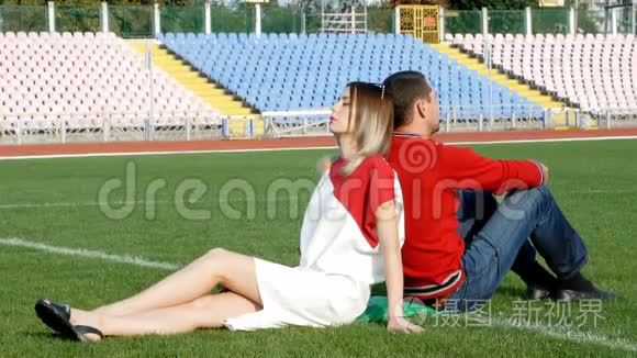 年轻人和漂亮的女孩坐在体育场足球场的中心