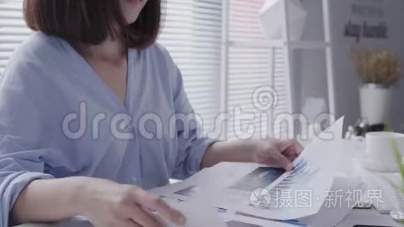 美丽的年轻拉斯特亚裔妇女，在家里坐在客厅里用笔记本电脑工作。 亚洲商界女性工作。