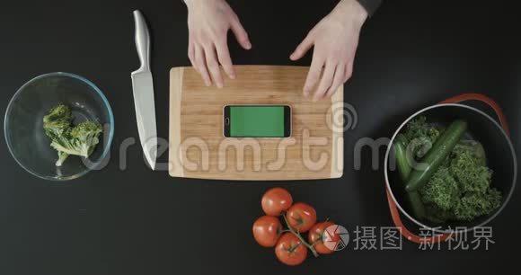双手握着电话上方的木切板靠近食物和大刀.. 上景。 绿色屏幕。