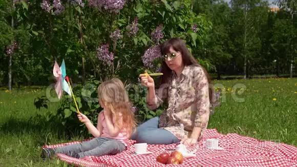 年轻的母亲和小女儿在春天的野餐旁边，一朵盛开的丁香花。
