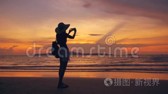 海洋海滩日落时分，戴帽子的年轻游客女士用手机拍照剪影
