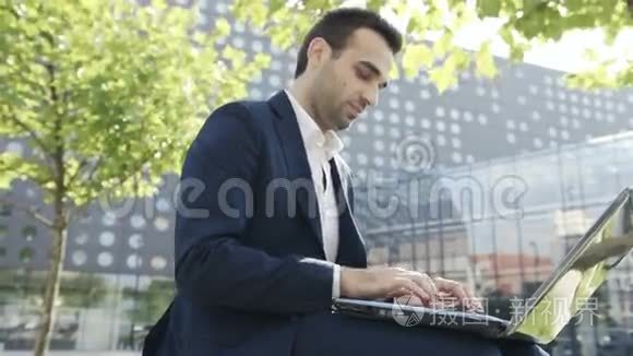 年轻商人坐在办公室附近的公园里，用笔记本电脑
