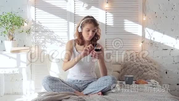 戴着耳机听着智能手机音乐在床上跳舞的快乐女人