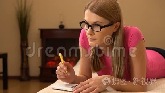 美丽迷人的年轻女子在笔记本上写作。 列个单子，想着又笑..