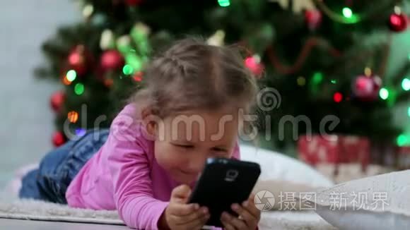 小可爱的女孩用智能手机，在圣诞树前。 特写镜头。