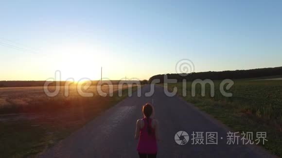运动慢跑的女人在日落时在田野附近跑步。