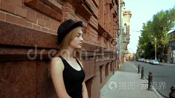 戴着黑帽子的漂亮金发女郎站在街上