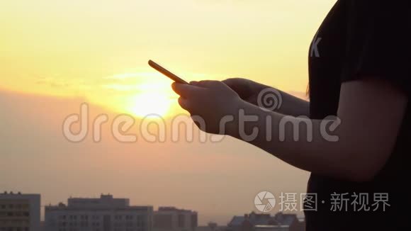 这个漂亮的女孩在一个建筑屋顶上的智能手机上写着这条信息。 晚上在高楼楼顶拍摄