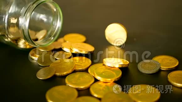 用黑桌上的金币和旋转的便士来特写静止的生活。 黄色的硬币从罐子里掉了出来。