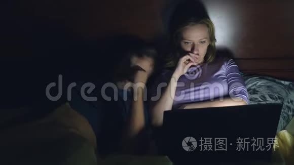 夫妻，男人和女人，在睡觉前在卧室的床上用笔记本电脑看电影。 看无聊的电影，摔倒