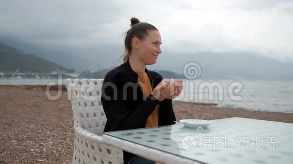 在一个女人的河岸上的咖啡馆里喝着温暖的饮料。