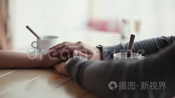 情侣手的特写.. 两只手牵着手，用勺子把空杯子放在桌子上。