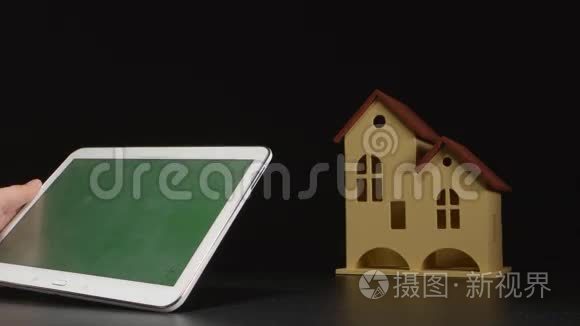 商人手中拿着一台平板电脑，靠近一张桌子上的房子模型（绿色屏幕）