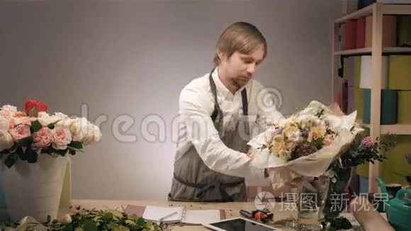 微笑的花匠站在花店里，捧着一束五颜六色的花。 有玫瑰花、豌豆、紫丁香和