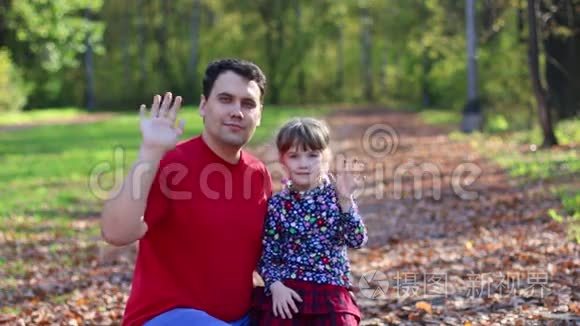 小女孩和她的父亲挥手，在阳光明媚的秋天公园玩耍