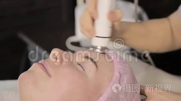 美丽的女人，闭着眼睛，把射频举在她的脸上。 在没有手术的情况下改善外观