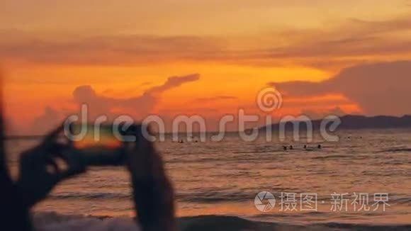 年轻的女游客在海滩日落时用智能手机拍摄海景