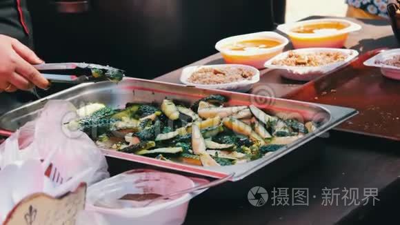 柜台上的女人用塑料盘子分发食物，里面有汤和粥。 附近有黄瓜