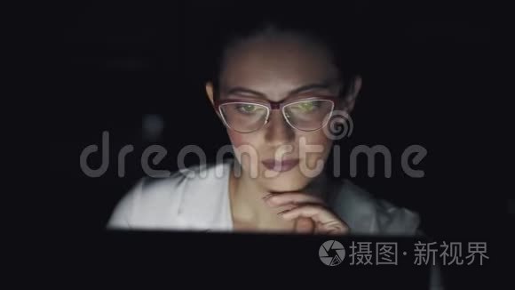 一个商务女性在笔记本电脑上工作到很晚的肖像。 带眼镜的屏幕反光