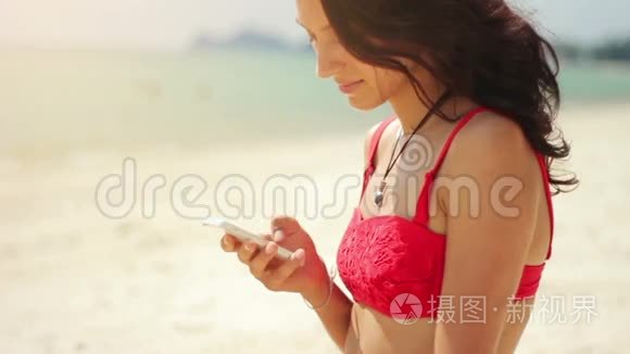 迷人的年轻女子在海滩上用手机视频