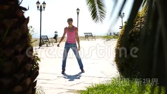 一个年轻快乐的家伙跳着现代芭蕾，在海边的背景下摇摇晃晃地走着。 缓行