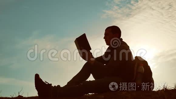 男学生在公园里背着背包看日落。 在天空生活方式日落时的人读书剪影